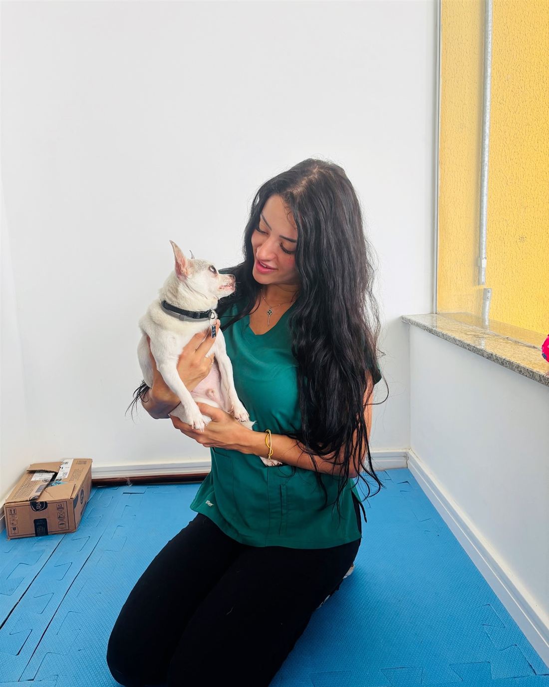 Dra. Kah segurando um cão pequeno no colo e olhando para ele com carinho